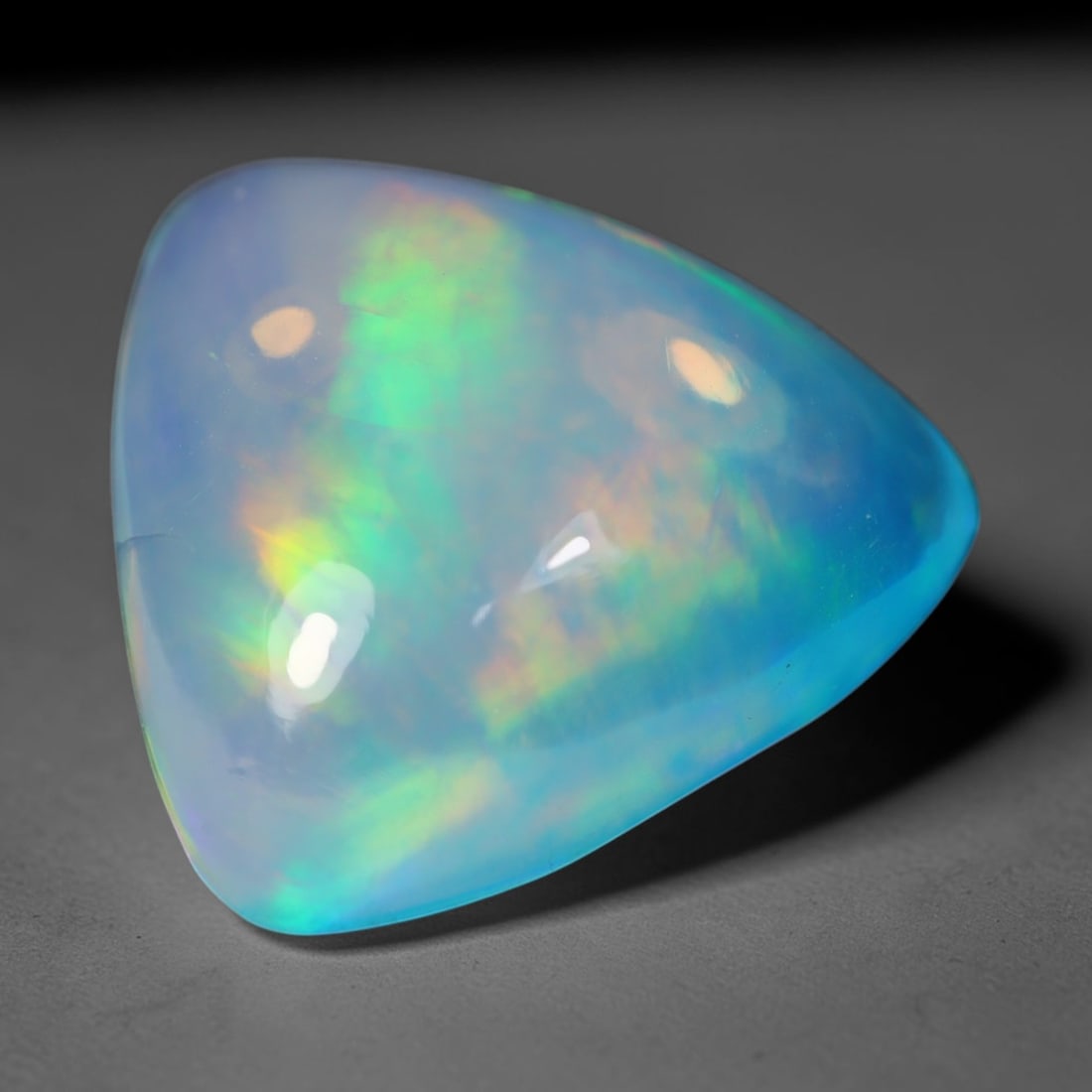 3.02 Carats Natural Ethiopian Welo Blue Trillion Cabochon Opal Loose Gemstone, 96WS: This smooth domed trillion cabochon Ethiopian Welo opal boasts a soft translucent sky-blue base with sweeping vivid play-of-color featuring lush lime green, golden yellow and faint orange iridescent f