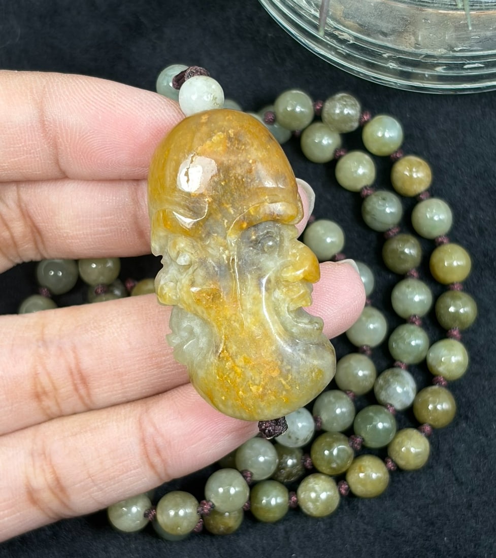 Burmese Jadeite Beaded Necklace with Hetian Jade Luohan Head Pendant, 72YJ: This necklace features a hand-carved Hetian jade luohan head pendant paired with natural Burmese jadeite round beads, strung on a brown cord. The pendant is crafted from Hetian jade with warm russet s