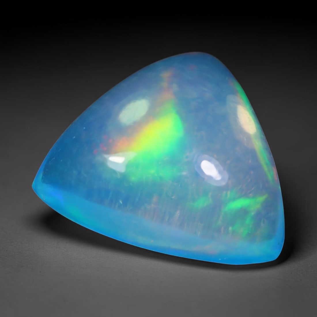 3.80 Carats Natural Ethiopian Welo Blue Trillion Cabochon Opal Loose Gemstone, 94WS: This smoothly polished domed trillion cabochon Ethiopian Welo opal features a soft translucent sky-blue base, decorated with vivid sweeping play-of-color including neon lime green, golden yellow and s