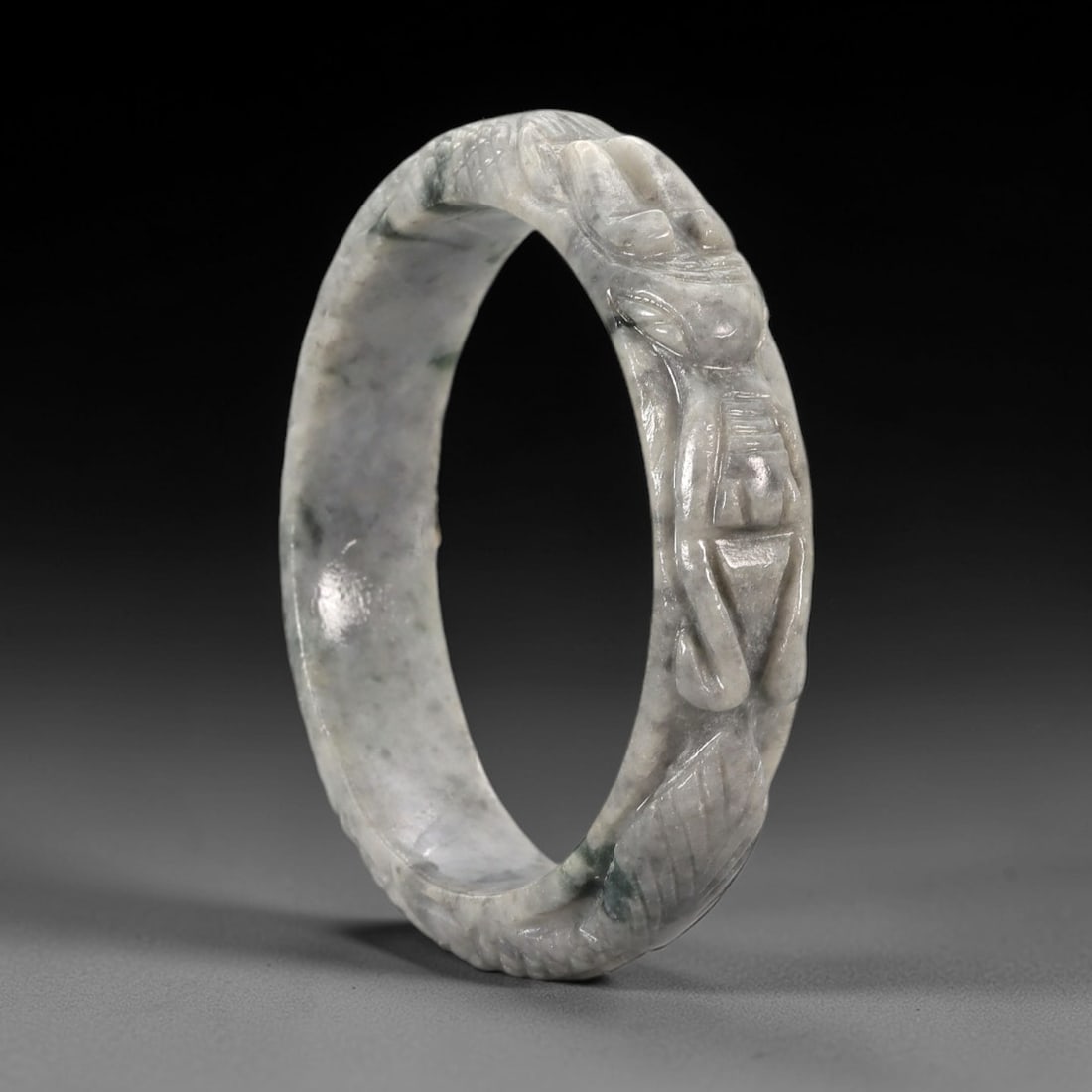 Natural Burmese Type A Carved Jadeite Jade Bangle Bracelet, 52ZL: A substantial jadeite bangle of circular form, masterfully carved in relief with a continuous band of a sinuous dragon coiling around its circumference. The stone exhibits a translucent pale white bas