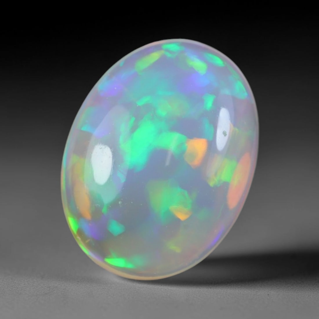 1.94 Carats Natural Ethiopian Welo Opal Oval Cabochon Loose Gemstone, 50XV: Natural Ethiopian Welo opal polished oval cabochon loose gemstone, luminous translucent milky white base stone with vivid multi-hued play-of-color featuring bright emerald green, lime yellow, soft blu