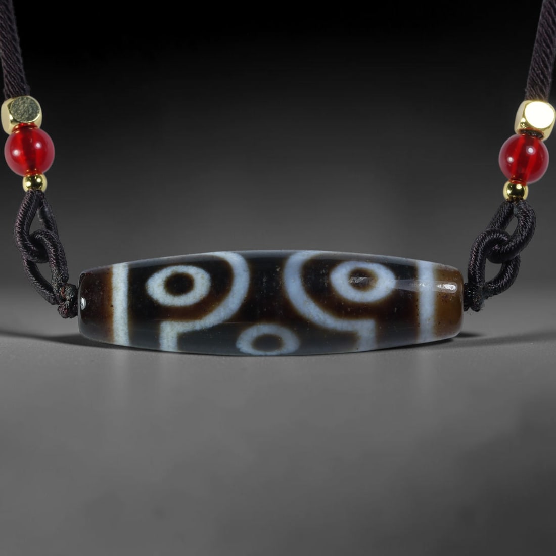 Vintage Tibetan Agate Dzi Bead Strung Pendant, 54YM: Crafted from natural agate with traditional surface patterning, this cylindrical bead has been pre-strung on a woven dark cord fitted with polished red glass accent beads and small metallic spacer bea