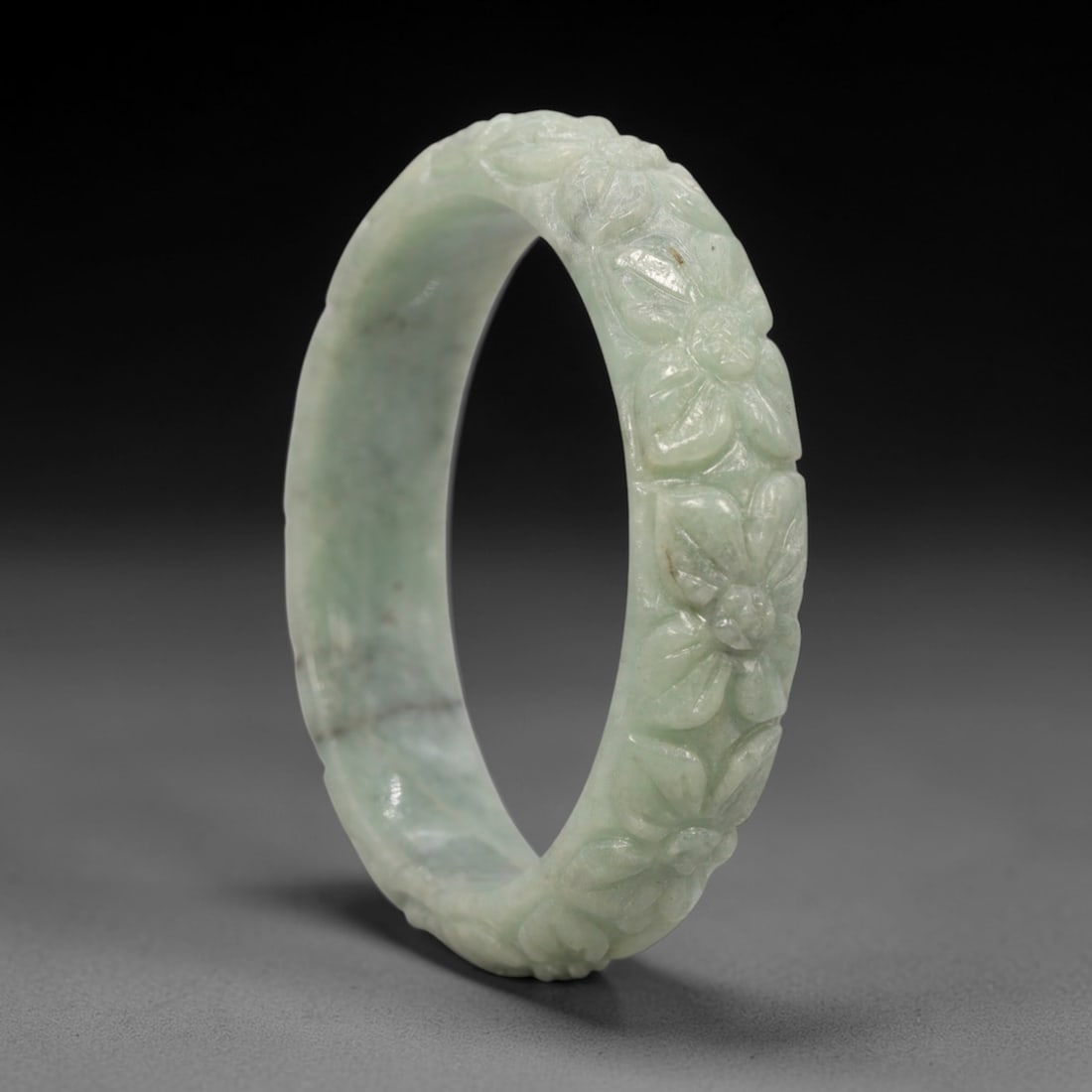 Natural Burmese Type A Carved Jadeite Jade Bangle Bracelet, 49ZL: A fine jadeite bangle of flattened circular form, masterfully carved in relief with a continuous band of floral blossoms and scrolling foliate motifs. The stone exhibits a translucent pale green base,