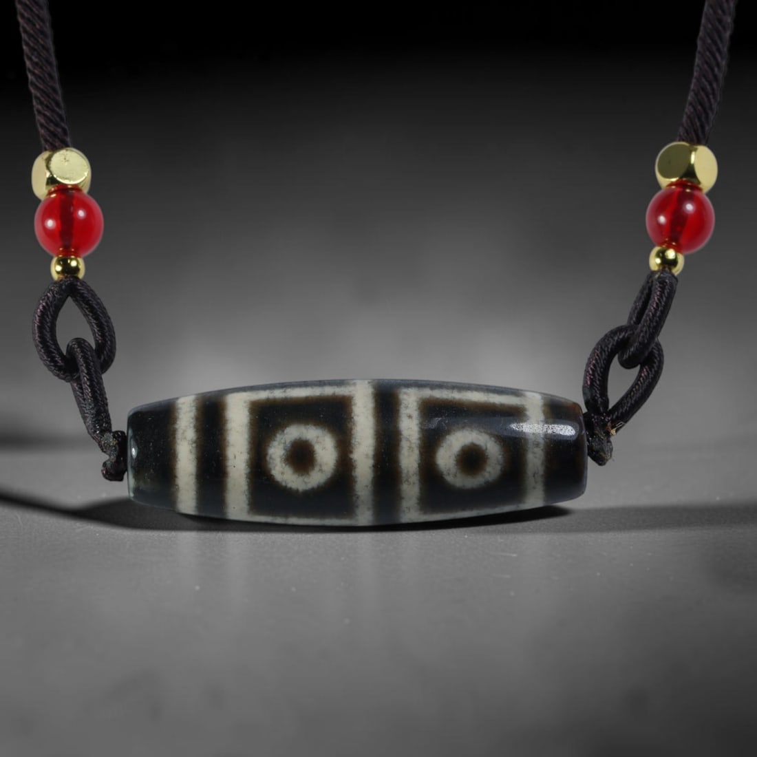 Vintage Tibetan Agate Dzi Bead Strung Pendant, 51YM: Crafted from natural agate with traditional surface patterning, this cylindrical bead has been pre-strung on a woven dark cord fitted with polished red glass accent beads and small metallic spacer bea