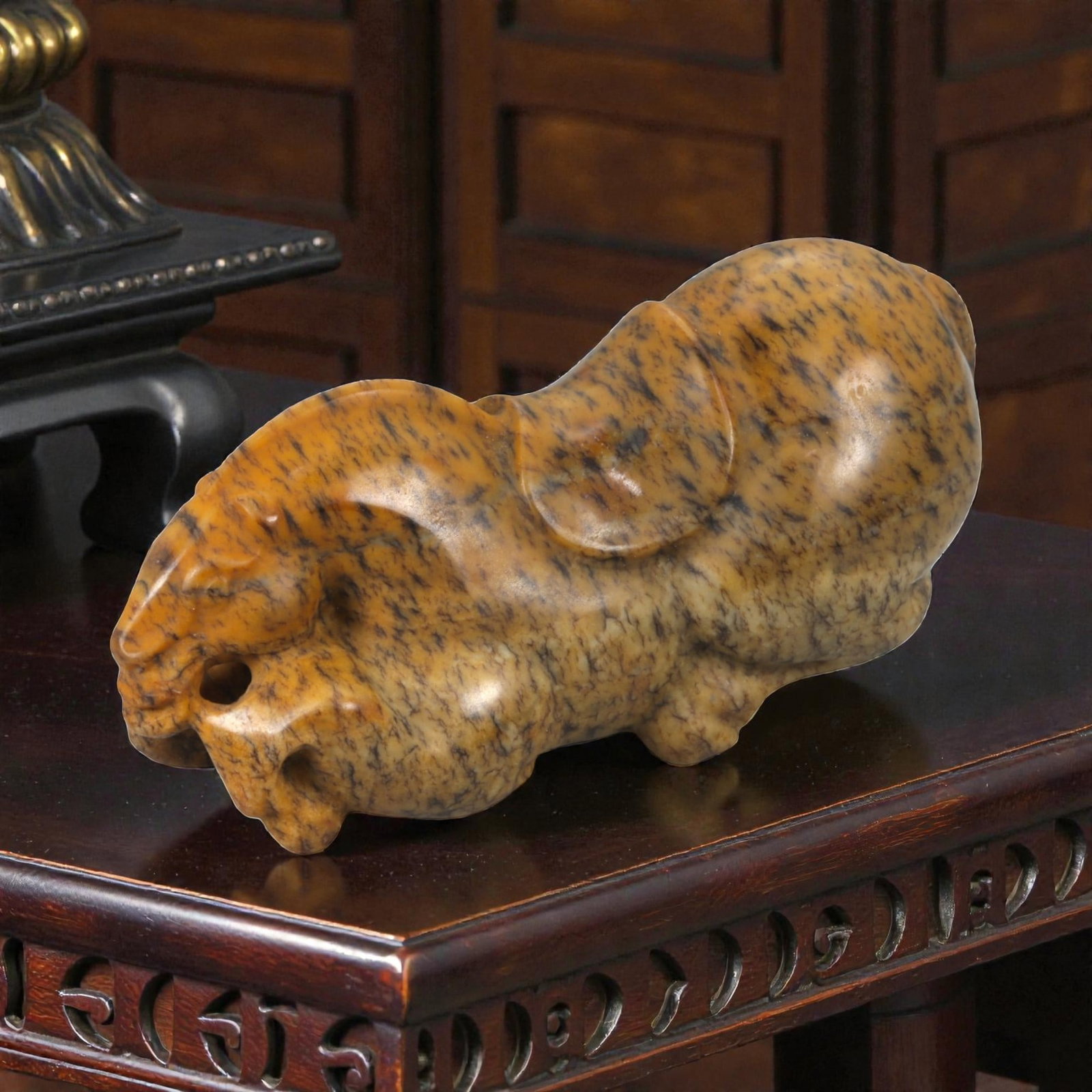 A Chinese Hardstone Recumbent Horse Figure, 20th Century, 84YA: Carved from mottled brown hardstone with dark veining and natural tonal variation, the figure is modeled in the round as a recumbent horse with legs folded beneath the body. The head is rendered with 