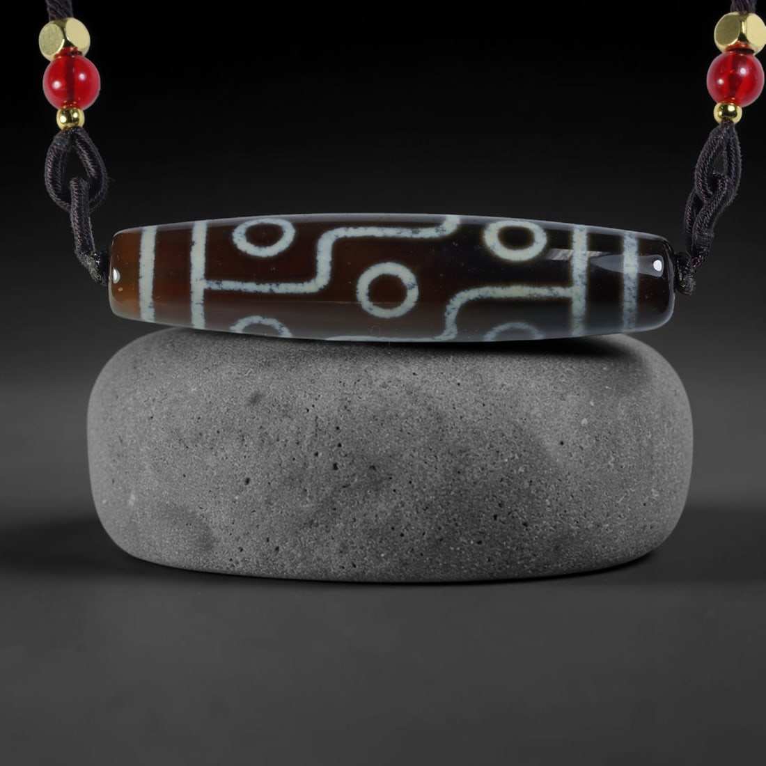Vintage Tibetan Agate Dzi Bead Strung Pendant, 57YM: Crafted from natural agate with traditional surface patterning, this cylindrical bead has been pre-strung on a woven dark cord fitted with polished red glass accent beads and small metallic spacer bea