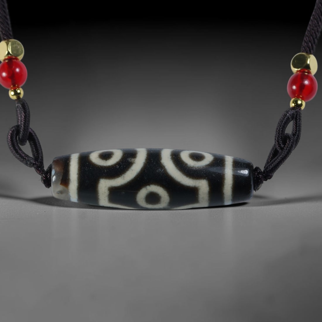 Vintage Tibetan Agate Dzi Bead Strung Pendant, 47YM: Crafted from natural agate with traditional surface patterning, this cylindrical bead has been pre-strung on a woven dark cord fitted with polished red glass accent beads and small metallic spacer bea