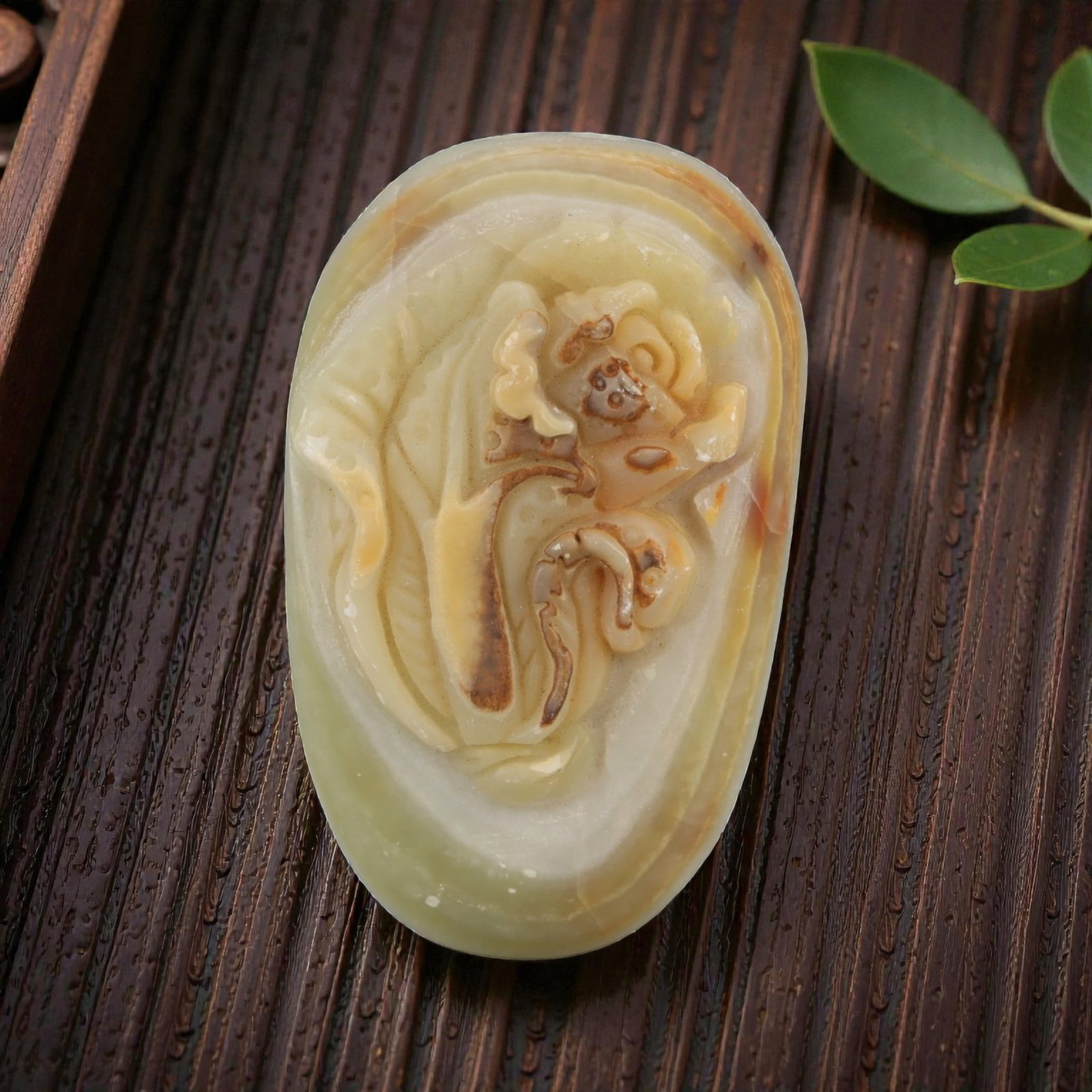 A Chinese Hardstone Pebble Carving, 20th Century, 64YB: Carved from a naturally shaped hardstone pebble with creamy beige, honey, and pale green tonal banding, worked in low relief and polished overall. One face is carved with a stylized floral composition