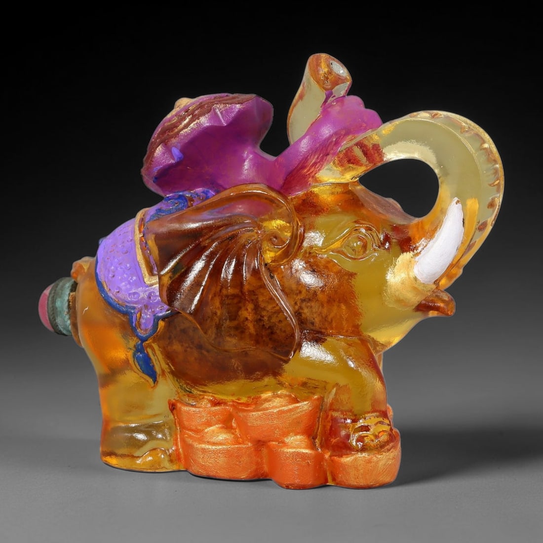 Vintage Chinese Liuli Glass Snuff Bottle - Treasure Elephant Figurine, 63YF: This snuff bottle is cast from translucent amber liuli glass and sculpted as a walking elephant with upturned trunk. The elephant stands atop gilded ingots, with a painted purple treasure sack on its 
