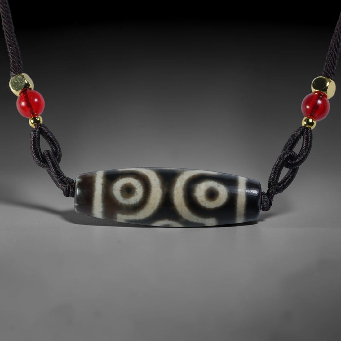 Vintage Tibetan Agate Dzi Bead Strung Pendant, 53YM: Crafted from natural agate with traditional surface patterning, this cylindrical bead has been pre-strung on a woven dark cord fitted with polished red glass accent beads and small metallic spacer bea
