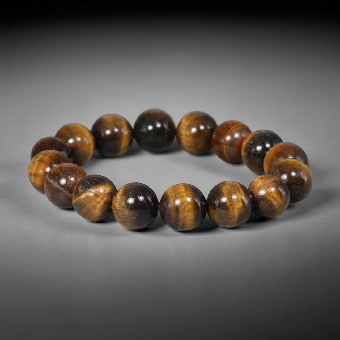 Tiger Eye Bead Bracelet - Polished Natural Stone Jewelry, 59YM: A bracelet composed of polished tiger's eye beads, exhibiting a rich chatoyant banding in golden brown, deep brown, and near-black tones. The beads are generally spherical with minor natural variation