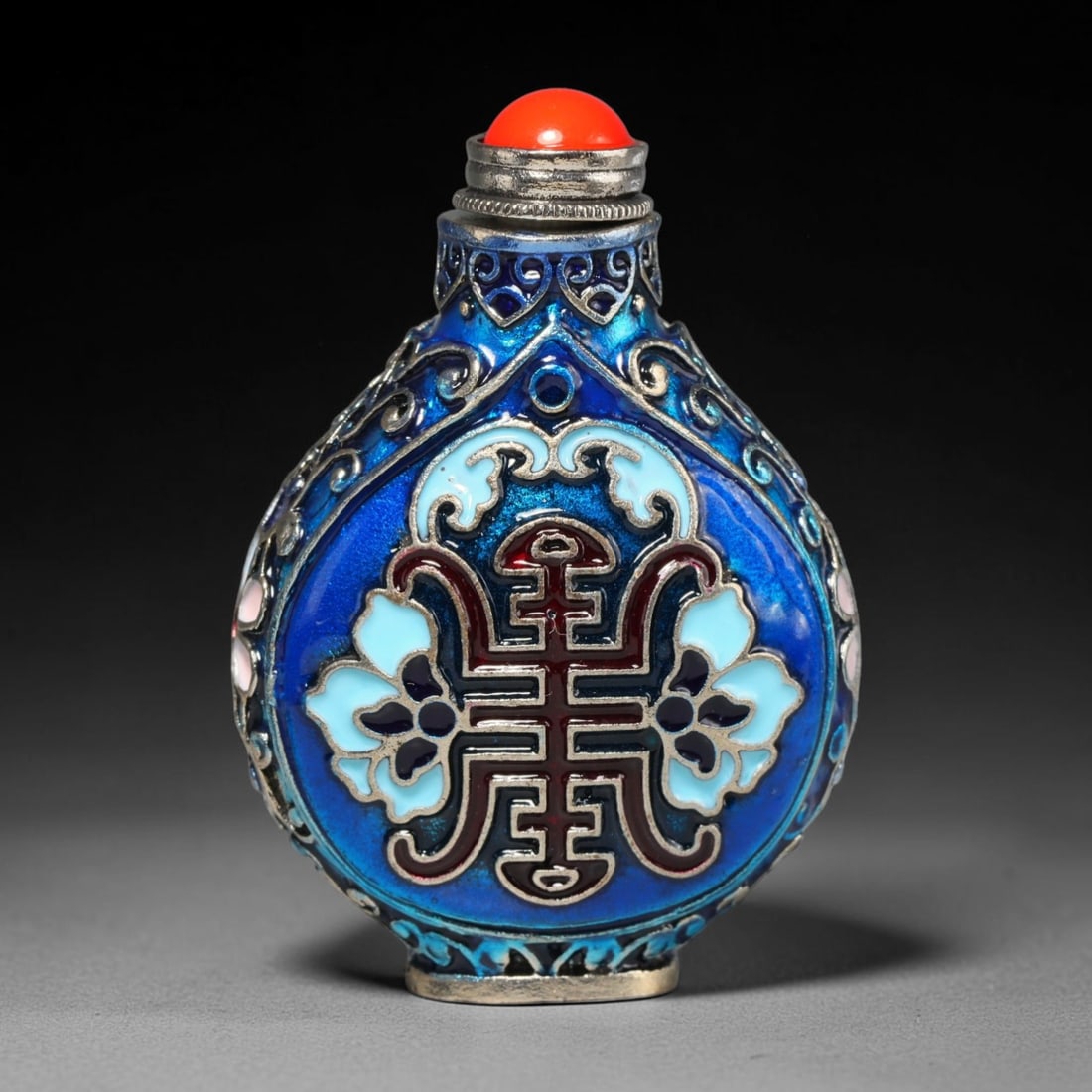 A Chinese Cloisonne Longevity Symbol Metal Snuff Bottle, 66WT: Forged from silver-toned base metal and finished with multi-toned cloisonne enamel work, the pear-shaped body is dominated by a central red longevity character framed by pale blue floral motifs agains