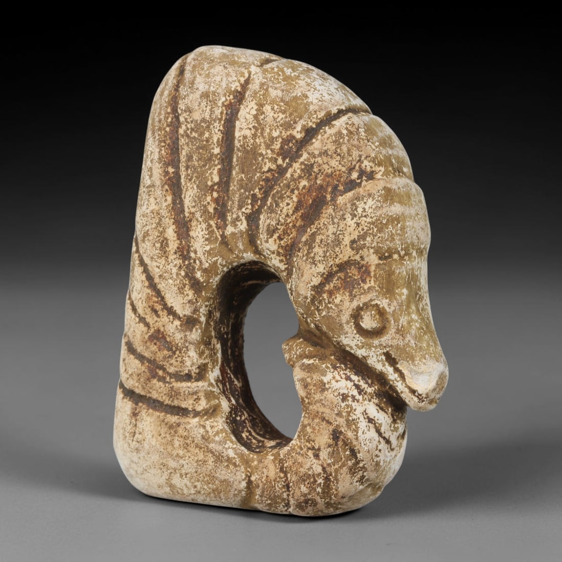 Ancient Medieval Near Eastern Tribal Stone Effigy, 90WT: Sculpted from weathered pale stone saturated with mottled aged earth patina, this tribal effigy takes the form of a coiled stylized animal figure with a large central open void running through its bod