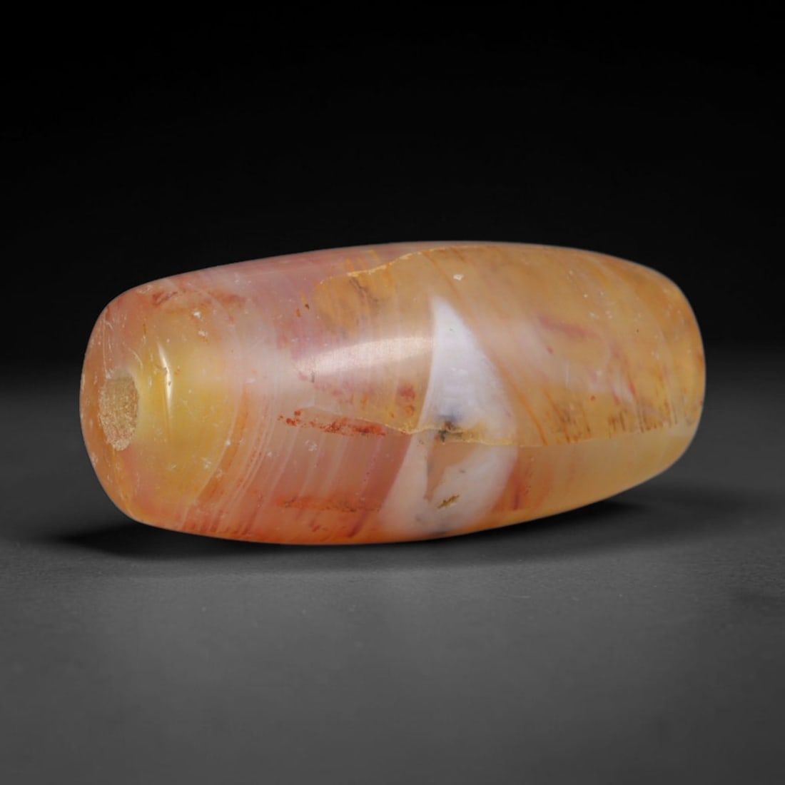Ancient Central Asian Steppe Carnelian Banded Chalcedony Mini Barrel Bead (800-200 BCE), 49XD: This miniature antique banded carnelian barrel bead originates from Eurasian steppe nomadic craft traditions, small portable hardstone talismans favored by caravan travelers and tribal elites for ligh