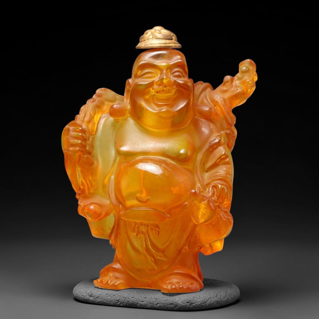 A Chinese Amber Resin Budai Figural Snuff Bottle, 65WT: Carved from translucent warm amber-hued resin, the vessel is fully modelled in the form of standing Budai with characteristic rounded belly, joyful facial expression and draped traditional robes. The 