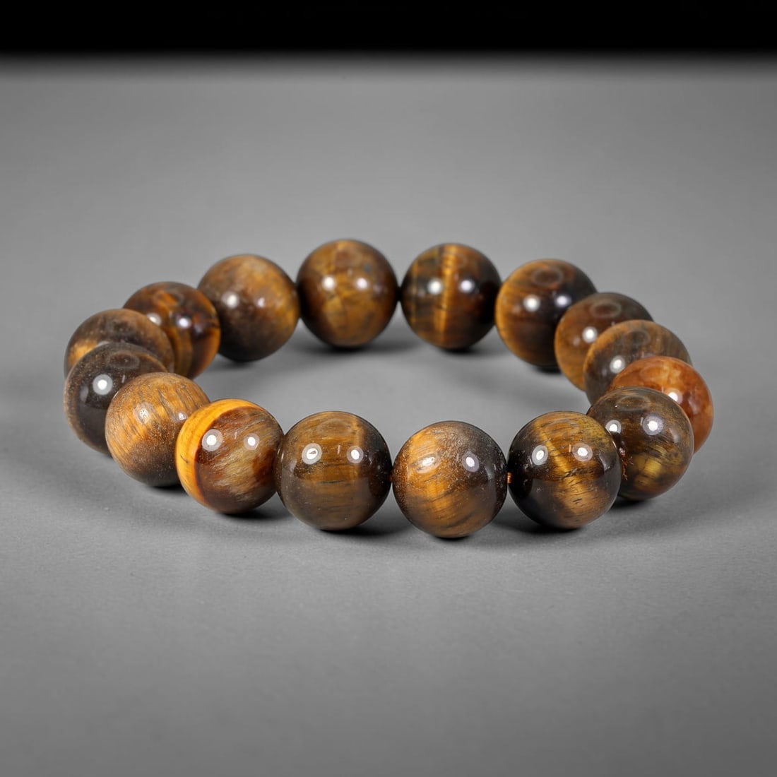 Tiger Eye Bead Bracelet - Polished Natural Stone Jewelry, 59XV: A bracelet composed of polished tiger's eye beads, exhibiting a rich chatoyant banding in golden brown, deep brown, and near-black tones. The beads are generally spherical with minor natural variation