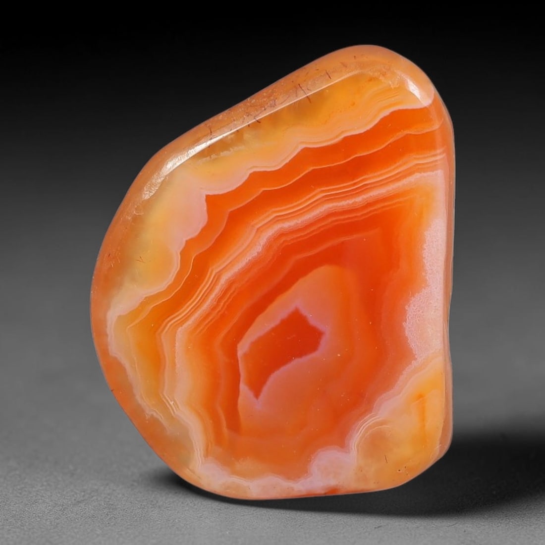 45ct Natural Brazilian Carnelian Banded Agate Sliced Rough Slab, 86YK: This polished slice specimen is natural carnelian banded agate sourced from Brazilian deposits, featuring concentric layered banding of rich orange, peach, and deep crimson-red chalcedony. One flat fa