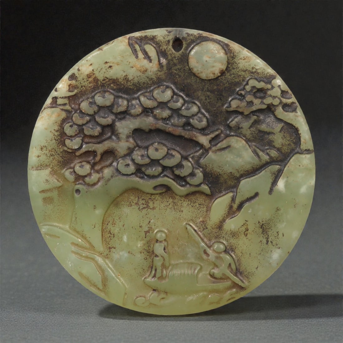 A Chinese Jade Landscape and Figure Disc Pendant, 41YA: Carved from pale green jade with extensive russet and dark brown surface staining accentuating the relief, the pendant is circular in form and worked in low relief on one face. The composition depicts