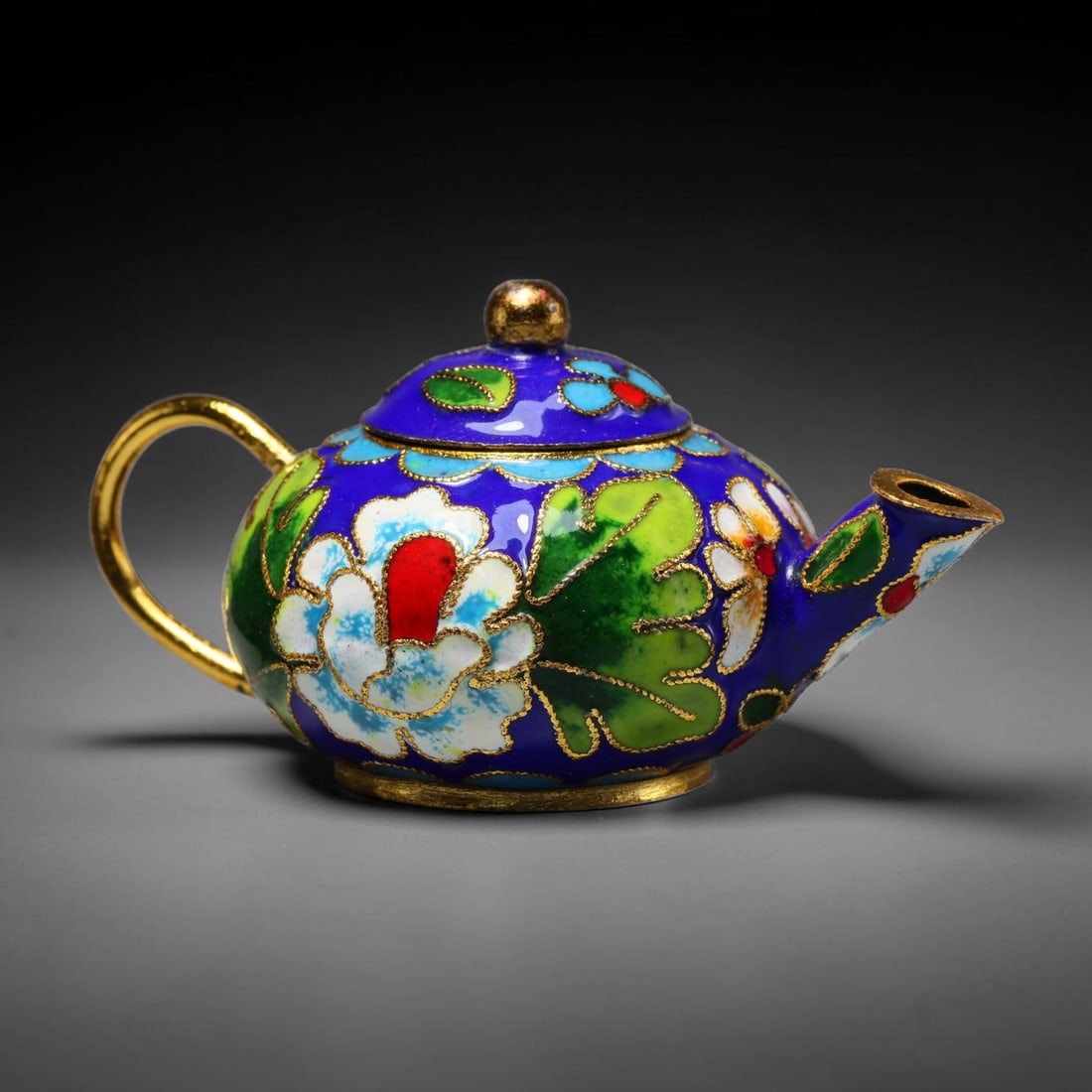 A Chinese Cloisonne Floral Miniature Teapot Ornament, 68WT: This small teapot is built upon a gilt metal framework detailed with fine copper wire cloisonne partitions filled with glossy deep blue enamel as the base ground. Large peony flowers with white petals