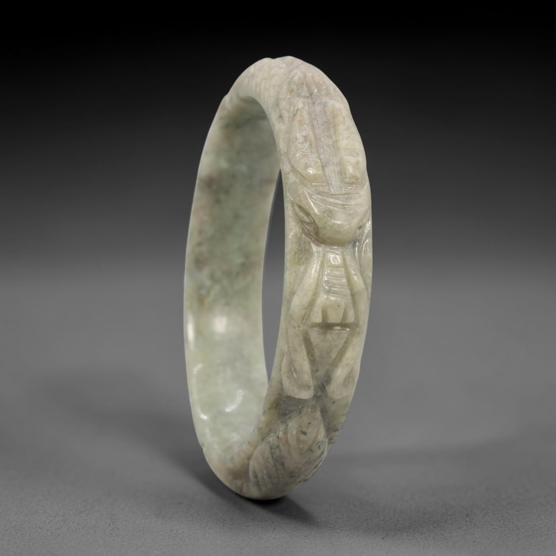 Natural Burmese Type A Carved Jadeite Jade Bangle Bracelet, 76ZL: A fine jadeite bangle of circular form, masterfully carved in relief with a continuous band of a sinuous dragon coiling around its circumference. The stone exhibits a translucent pale green base, with