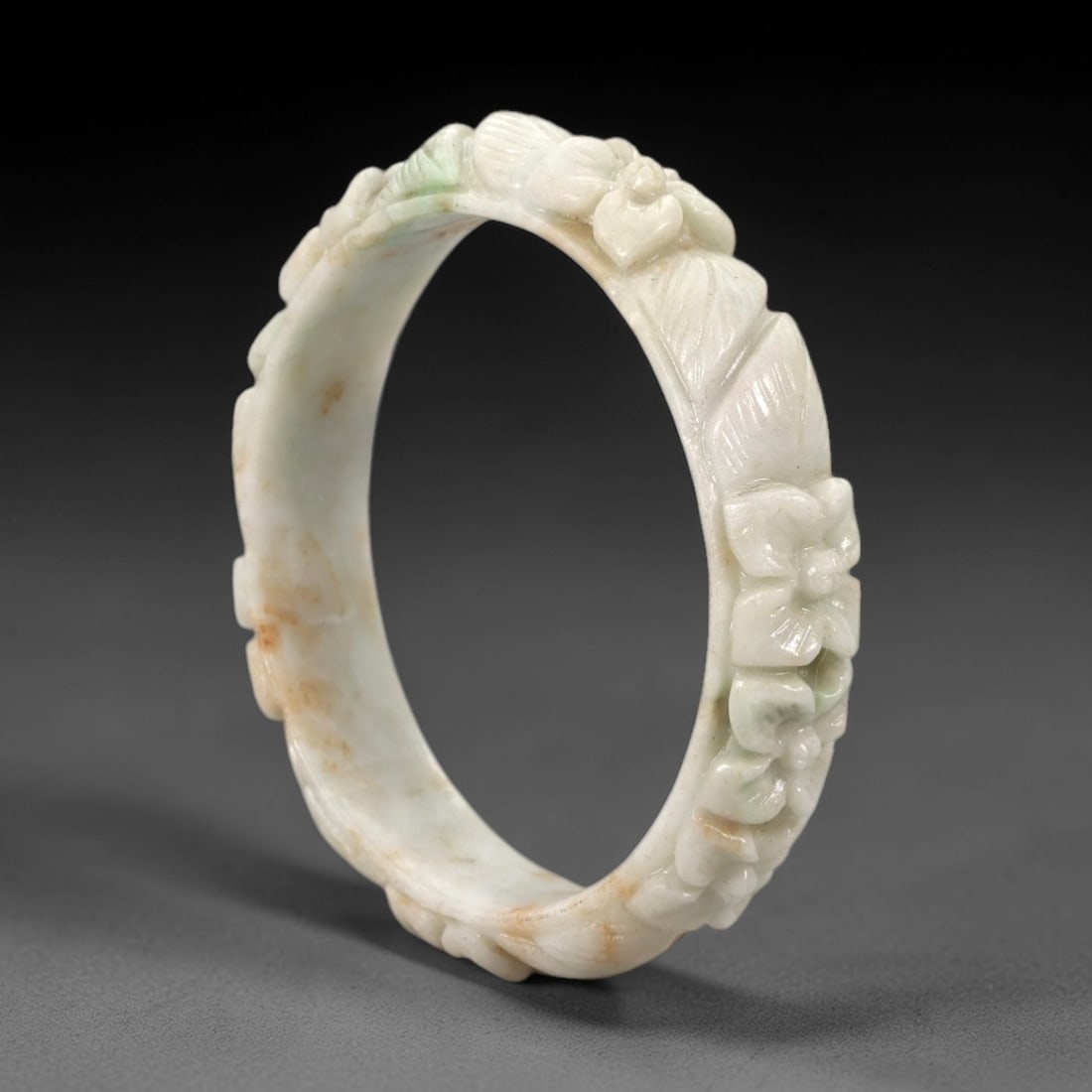 Natural Burmese Type A Carved Jadeite Jade Bangle Bracelet, 57ZL: A delicately proportioned jadeite bangle of flattened circular form, carved in mid-relief with a continuous band of stylized floral sprays and foliate motifs. The stone features a soft milky-white bas