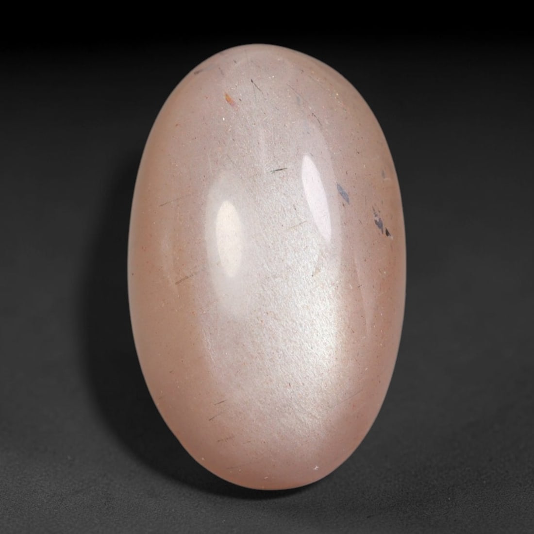 10.56 Carats Natural Ceylon Peach Fibrous Inclusion Moonstone Oval Cabochon Loose Gemstone, 81WS: This soft peach blush Ceylon moonstone oval cabochon holds a translucent warm pale pink feldspar matrix streaked with scattered fine dark fibrous needle inclusions and minor flake mineral deposits thr