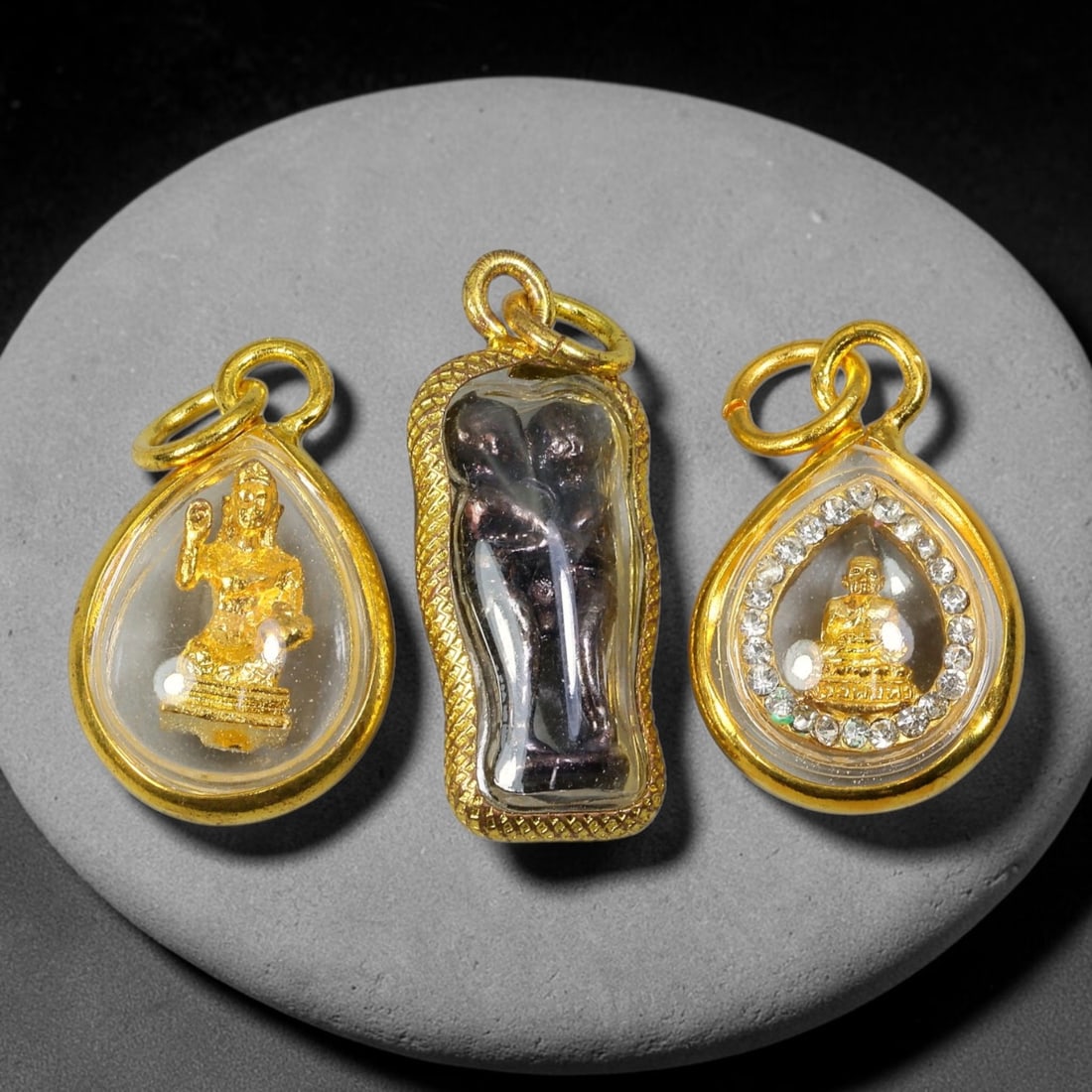 Set of 3 Assorted Dual-Sided Thai Gold Cased Amulet Pendants, 29YY: A curated three-piece collection of distinct Thai spiritual amulets, each sealed within polished gold casings fitted with clear transparent dome covers and double-loop gold hanging rings, all featurin