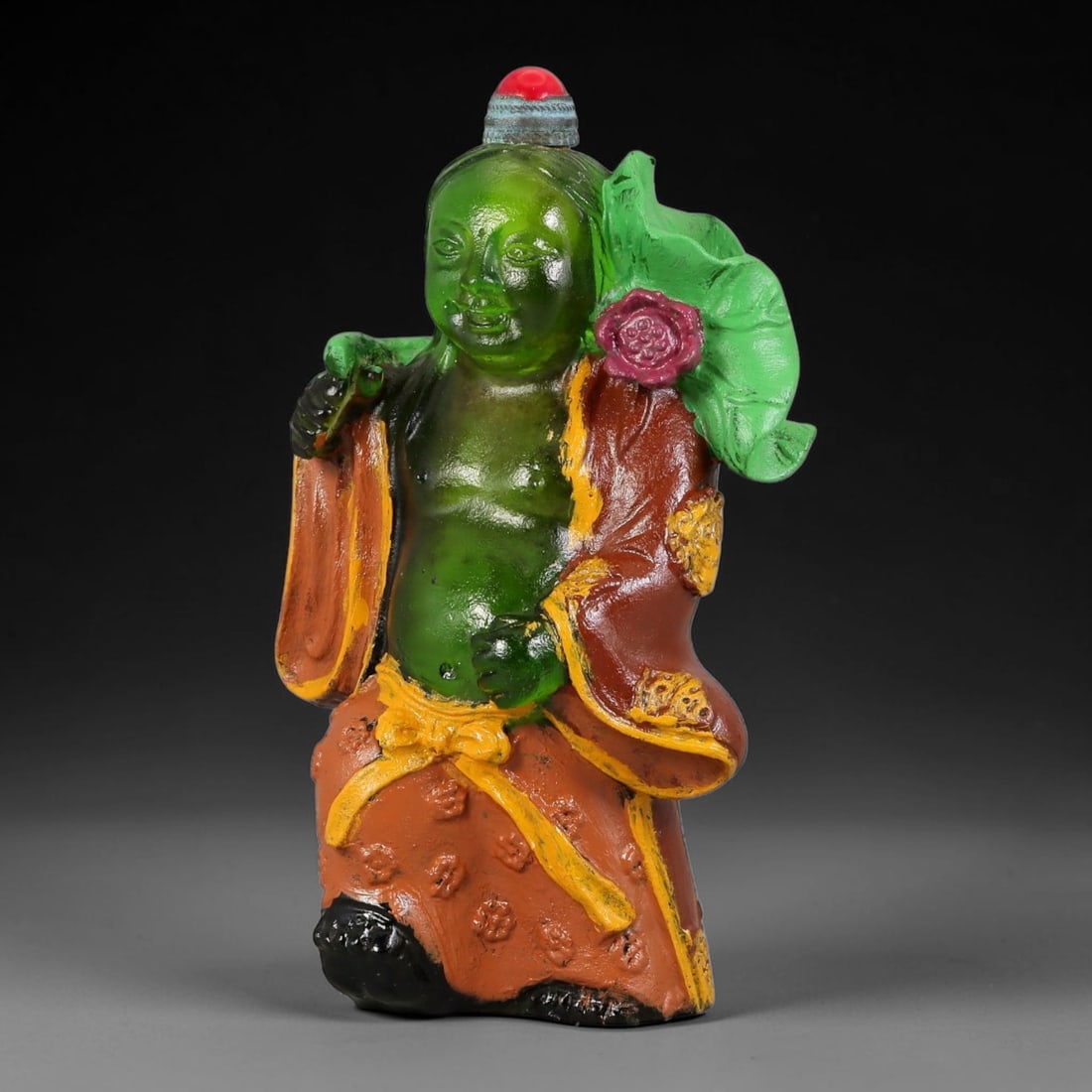Vintage Chinese Liuli Glass Snuff Bottle - He-He Immortal with Lotus Leaf, 79YF: This snuff bottle is moulded from translucent green liuli glass and shaped as a smiling He-He immortal. The figure carries a large lotus leaf with a pink blossom over one shoulder, wearing a layered r