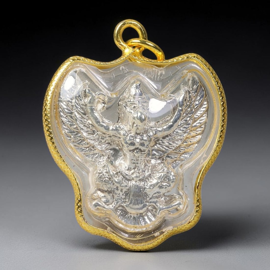 Thai Gold Frame Silver Garuda Amulet Pendant With Clear Protective Casing, 63YY: Unique bat-wing shaped textured gold plated casing amulet sized 3.5x3.0cm, equipped with dual gold jump rings for necklace threading. A transparent sealed dome protects the inner silver-toned Garuda s