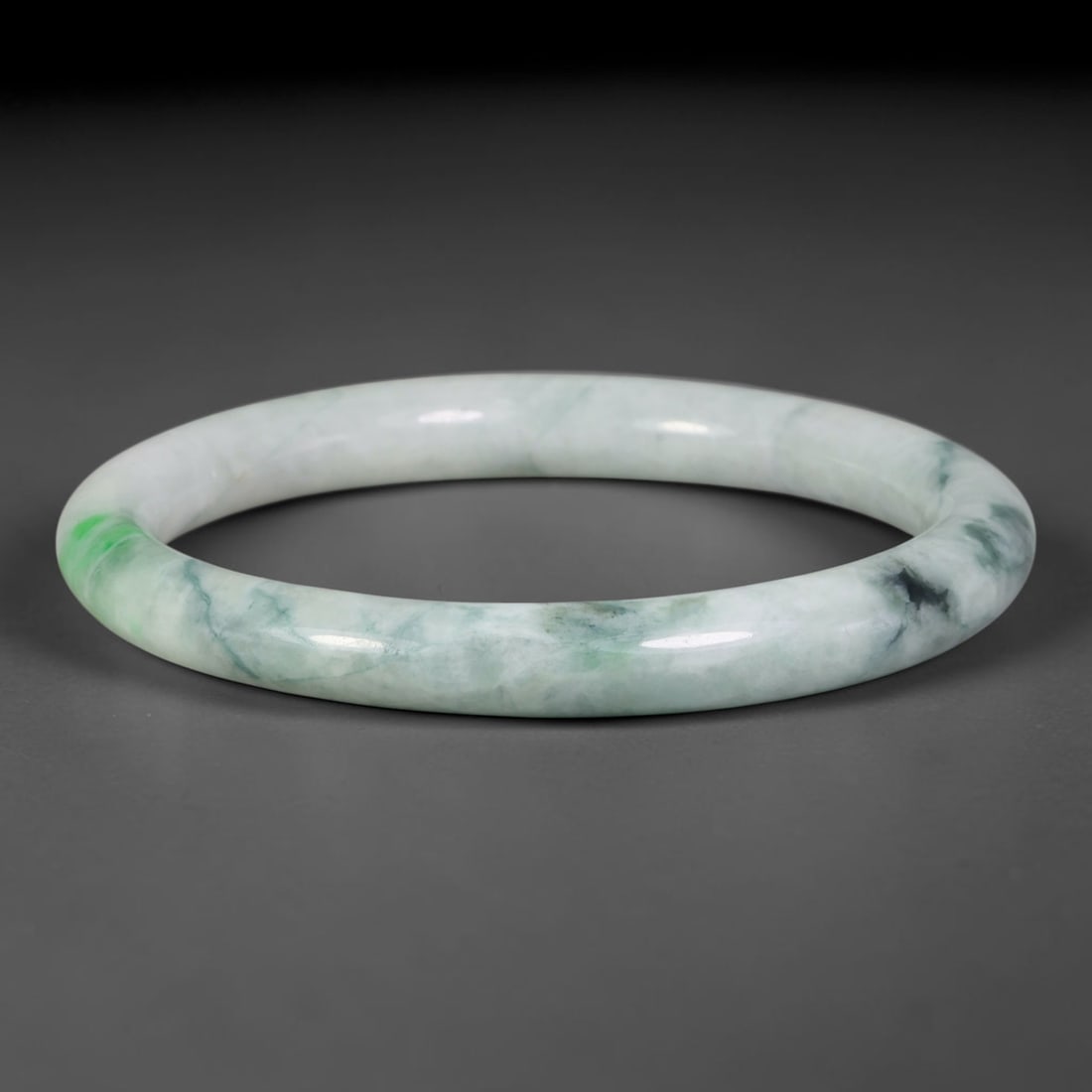 Natural Burmese Type A Jadeite Jade Bangle Bracelet, 12TD: Formed of natural Burmese type-A jadeite, this rounded bangle holds a pale milky-white foundation accented by a distinct bright lime-green patch at one end, alongside wispy dark green-black flowing ve