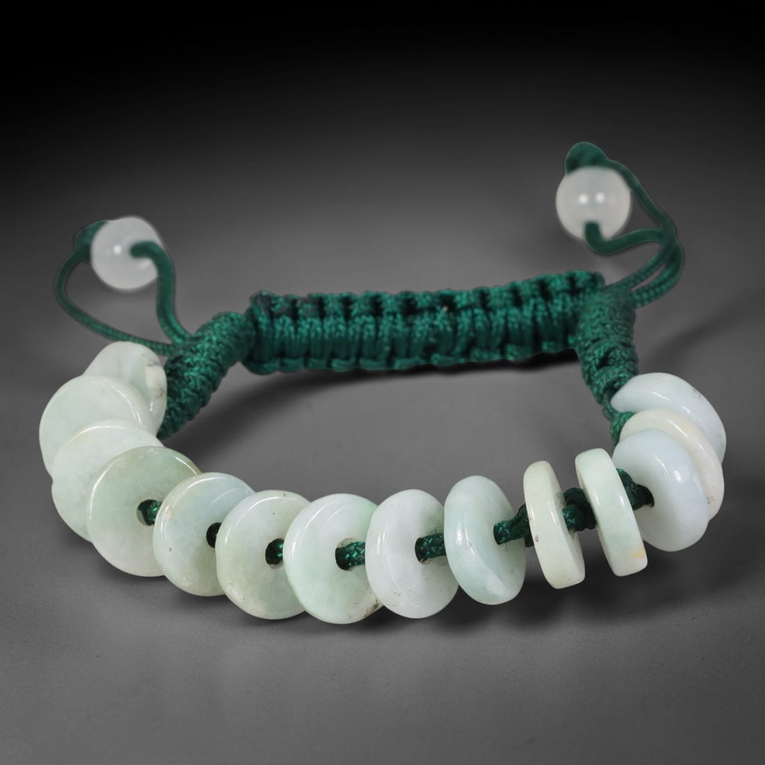 Natural Burmese Type A Pale Green Donut Jadeite Jade Adjustable Braided Bracelet, 60TA: Constructed from untreated natural Burmese Type A pale green jadeite, this bracelet features uniform flat circular donut beads measuring 10.6 millimeters each, strung upon densely woven deep green tex