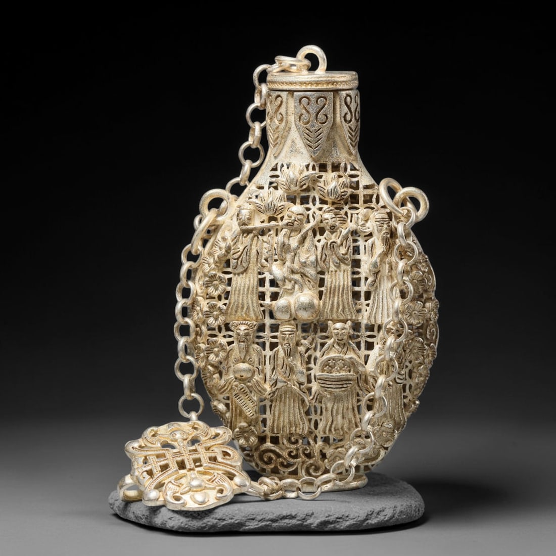 A Chinese Openwork Metal Snuff Bottle - Eight Immortals Figural Vessel, 63WT: Formed from silver-toned base metal with intricate pierced openwork filigree composing the main body lattice, the structure is adorned with sculpted eight immortals encircled by blooming floral scroll