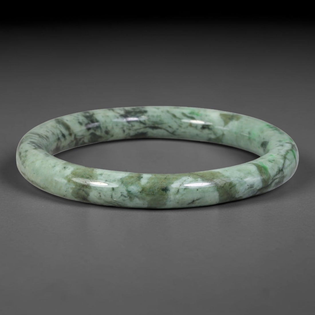 Natural Burmese Type A Jadeite Jade Bangle Bracelet, 14TD: Made from natural Burmese type-A jadeite, this bangle presents a muted pale sage-green base layered with rugged mottled forest-green and dark mineral veining traversing the full circumference. The ban