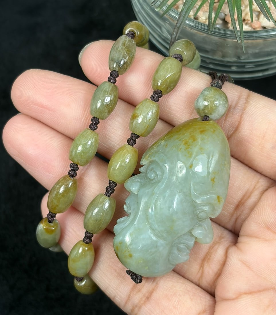 Burmese Jadeite Beaded Necklace with Hetian Jade Luohan Head Pendant, 71YJ: This necklace features a hand-carved Hetian jade luohan head pendant paired with natural Burmese jadeite pebble beads, strung on a brown cord. The pendant is crafted from Hetian jade with subtle russe