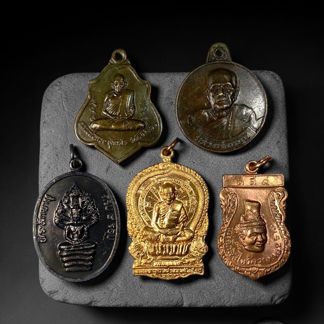 Thai Vintage Mixed Metal Buddhist Monk Amulets - 5pcs Set, 21YZ: This five-piece collection features vintage Thai devotional pendants cast from varied copper, brass, and dark alloy metals, each fitted with an integral suspension loop for wear. Obverse faces bear em