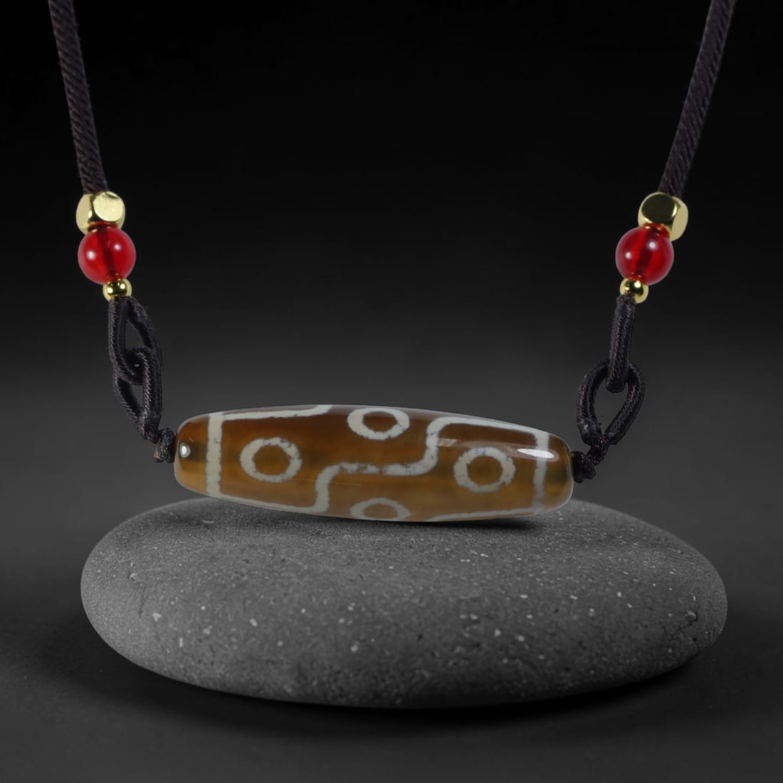 Vintage Tibetan Agate Dzi Bead Strung Pendant, 50YM: Crafted from natural agate with traditional surface patterning, this cylindrical bead has been pre-strung on a woven dark cord fitted with polished red glass accent beads and small metallic spacer bea