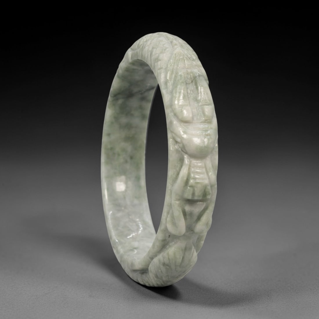 Natural Burmese Type A Carved Jadeite Jade Bangle Bracelet, 22ZL: A fine jadeite bangle of circular form, masterfully carved in relief with a continuous band of a sinuous dragon coiling around its circumference. The stone exhibits a translucent pale green base, with