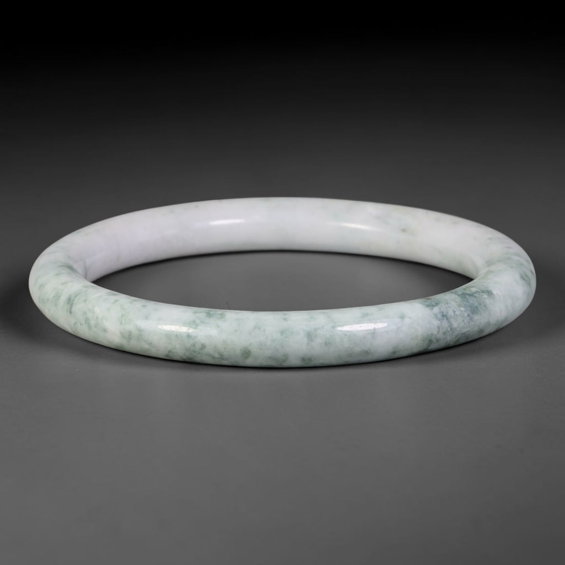 Natural Burmese Type A Jadeite Jade Bangle Bracelet, 17TD: Crafted from natural Burmese type-A jadeite, this rounded bangle displays a clean milky-white base softly mottled with scattered light sage-green clouded inclusions concentrated along the lower hoop. 