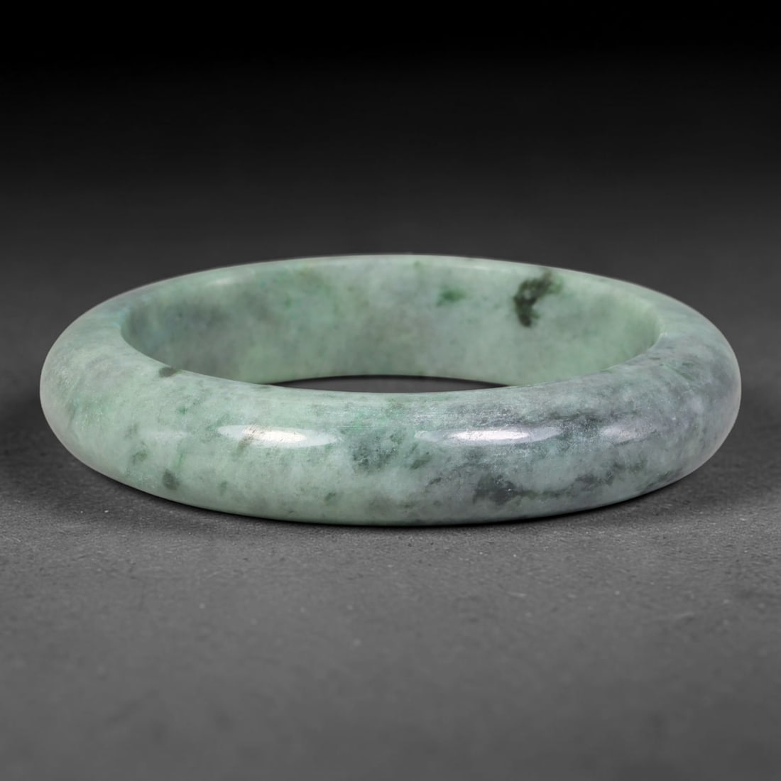Natural Burmese Type A Pale Sage Speckled Floating Green Jadeite Jade Bangle Bracelet, 69TD: Polished from natural Burmese jadeite, this solid bangle features a soft pale sage green base naturally scattered with dark green and grey mineral speckling across the stone matrix. Formed in a tradit