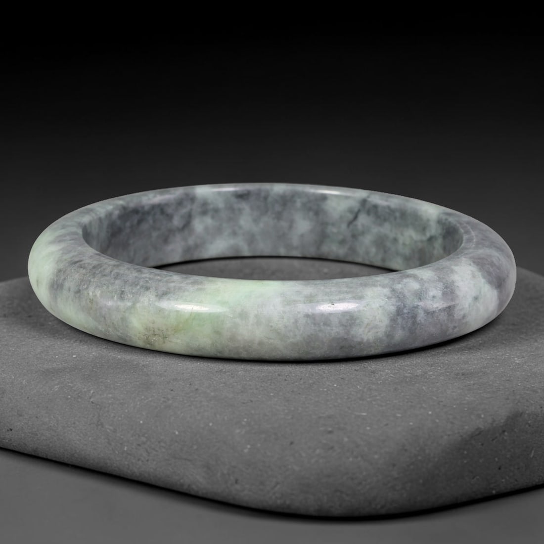 Natural Burmese Type A Grey Mottled Floating Green Jadeite Jade Bangle Bracelet, 70TD: Polished from natural Burmese jadeite, this solid bangle features a blended grey mottled base accented by a soft patch of pale floating green within the matrix. Formed in a traditional rounded bangle 
