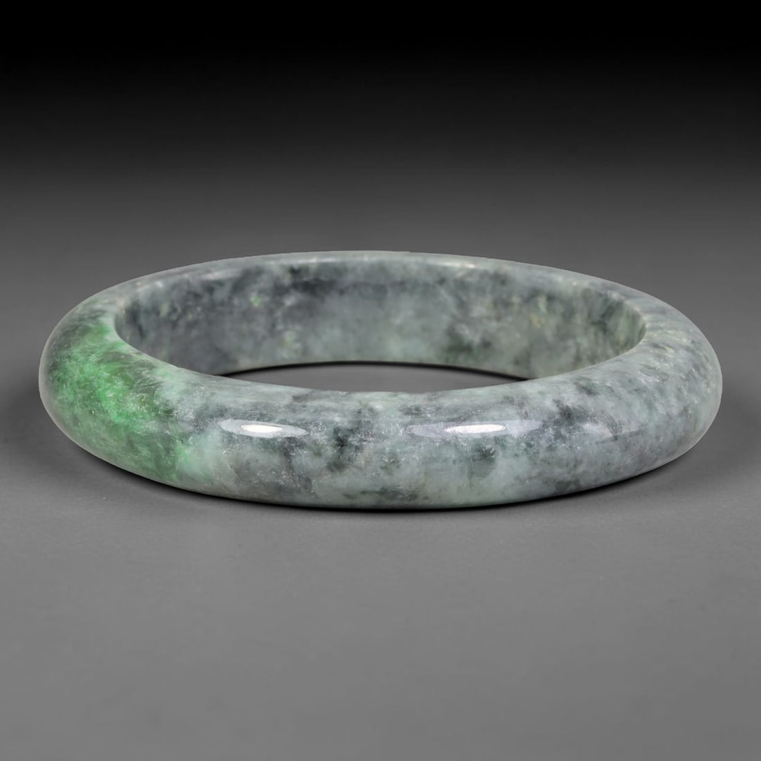 Natural Burmese Type A Dark Speckled Floating Green Jadeite Jade Bangle Bracelet, 71TD: Polished from natural Burmese jadeite, this solid bangle features a muted greyish base densely mottled with dark mineral speckling, accented by a concentrated band of vivid floating green along one si