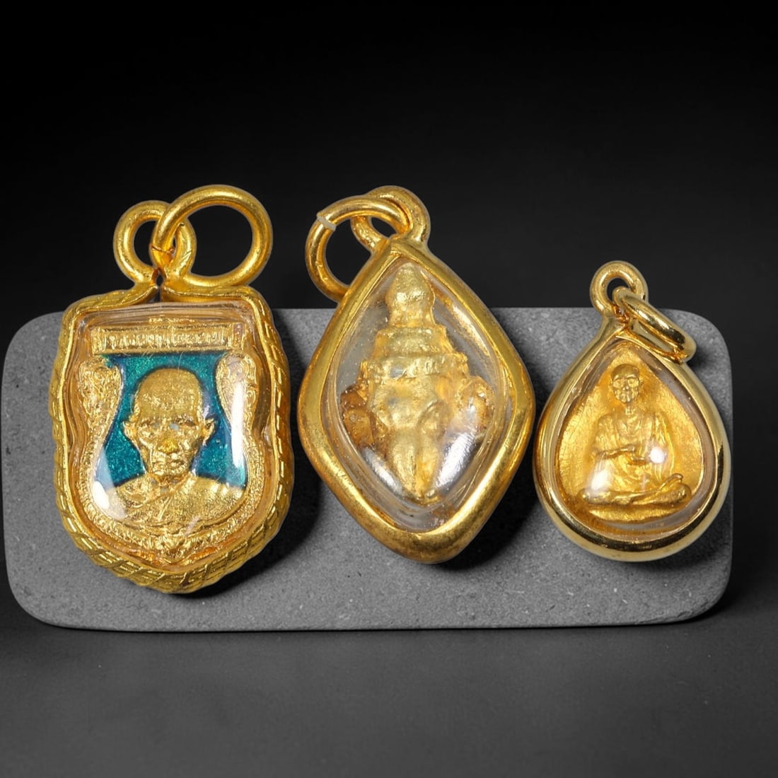 Set of 3 Assorted Thai Gold Cased Amulets Mini Monk & Ganesha Votive Pendants, 27YY: A curated set of three distinct miniature Thai spiritual amulets, all sealed inside polished gold engraved casings with clear transparent dome covers and double loop gold hanging bails. The largest pi