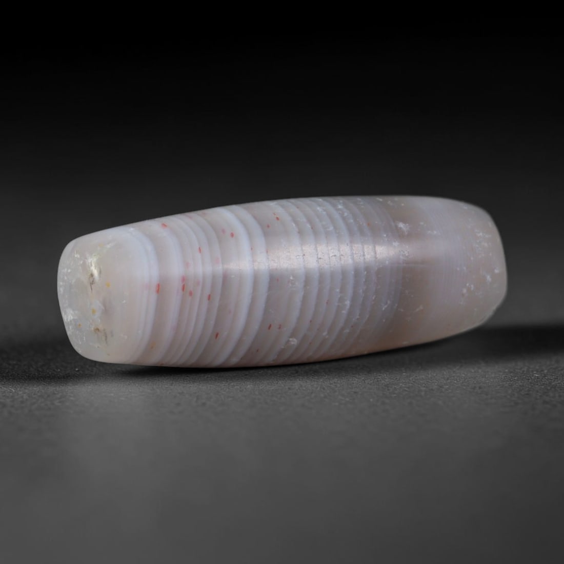 Ancient Sogdian Slender White Banded Agate Mini Barrel Trade Bead (500-1000 CE), 40XD: This delicate elongated banded agate barrel bead was crafted by Sogdian caravan artisans, makers of slim lightweight chalcedony talismans ideal for layering into fine necklaces traded across the full 