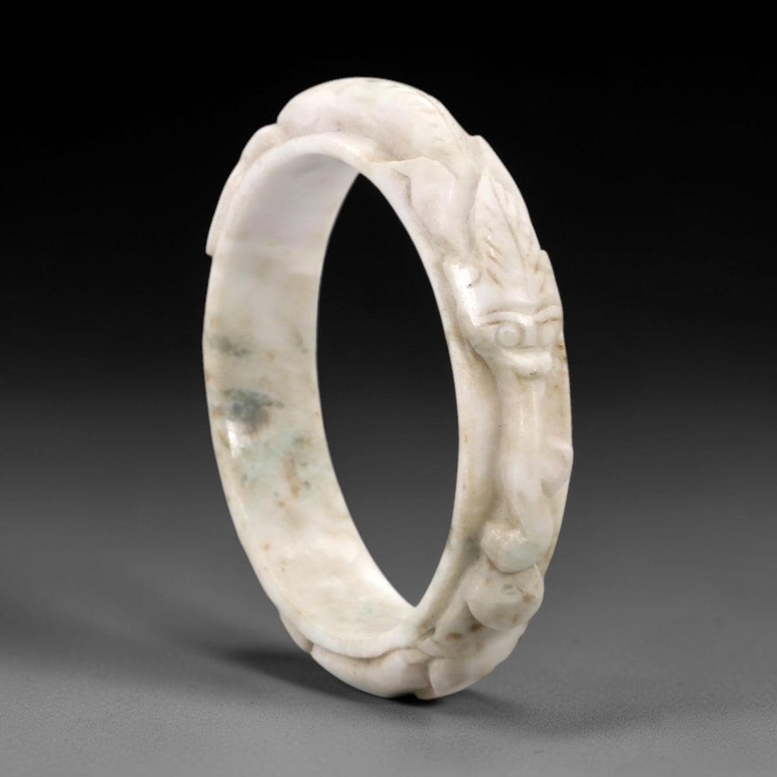 Natural Burmese Type A Carved Jadeite Jade Bangle Bracelet, 38ZL: A fine jadeite bangle of flattened circular form, masterfully carved in relief with a continuous band of a sinuous dragon coiling around its circumference. The stone exhibits a creamy white base, acce