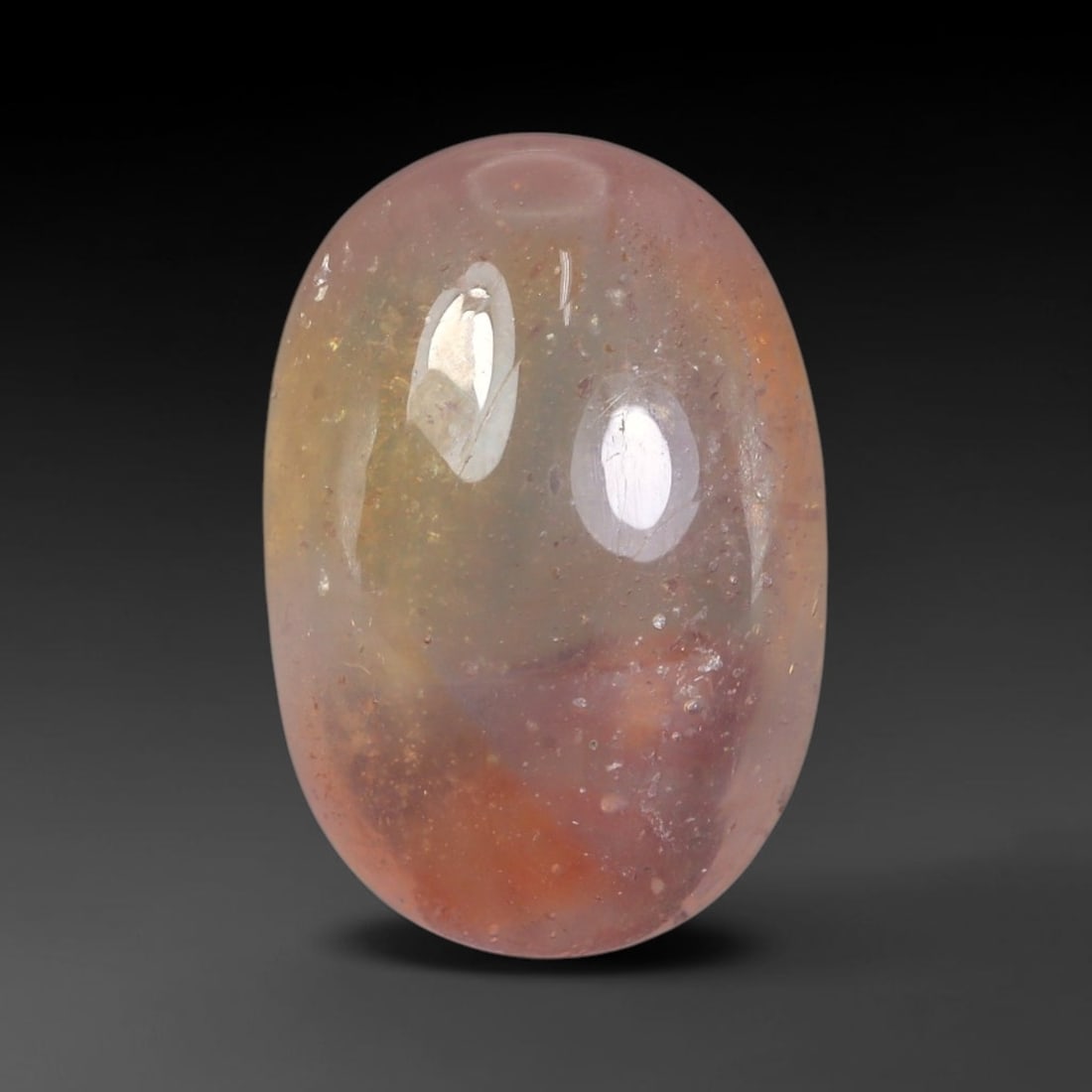 12.67 Carats Natural Multi-Tone Pastel Sapphire Oval Cabochon Loose Gemstone, 99WC: This sleek oval cabochon sapphire displays a stunning natural blended color gradient, shifting from soft milky pale lavender-pink through muted golden honey tones down to warm rust orange at the base.