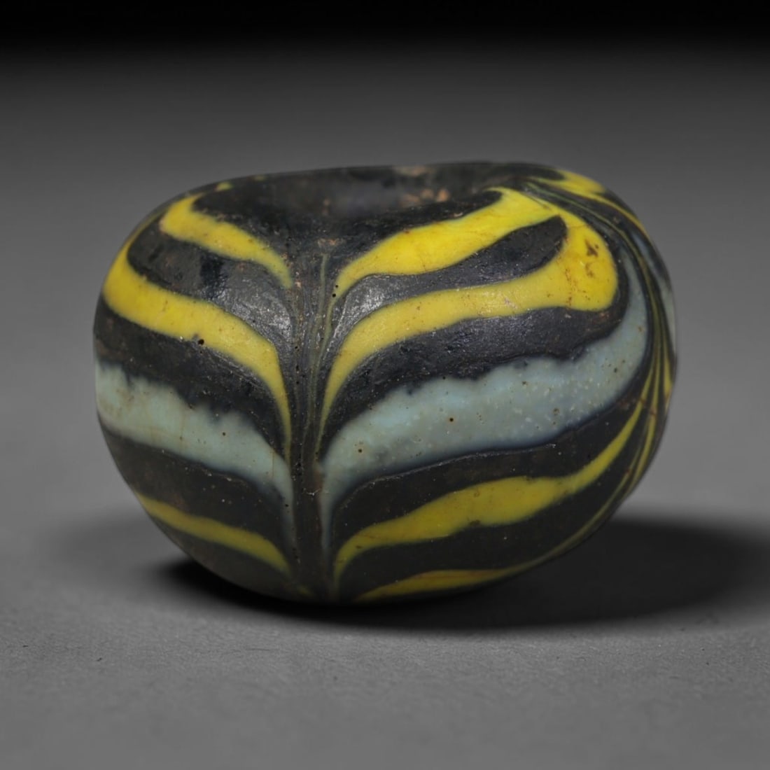 Ancient Islamic Hand Crafted Glass Bead Talisman, 28XD: Miniature antique wearable bead formed from hand-worked glass material, originating from ancient Islamic period glassmaking traditions across the Near East and North African cultural spheres. Glass wa