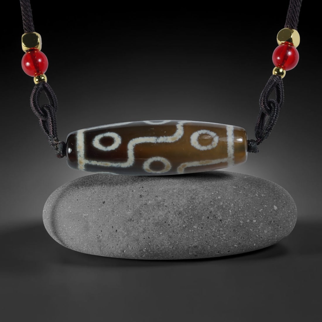 Vintage Tibetan Agate Dzi Bead Strung Pendant, 55YM: Crafted from natural agate with traditional surface patterning, this cylindrical bead has been pre-strung on a woven dark cord fitted with polished red glass accent beads and small metallic spacer bea