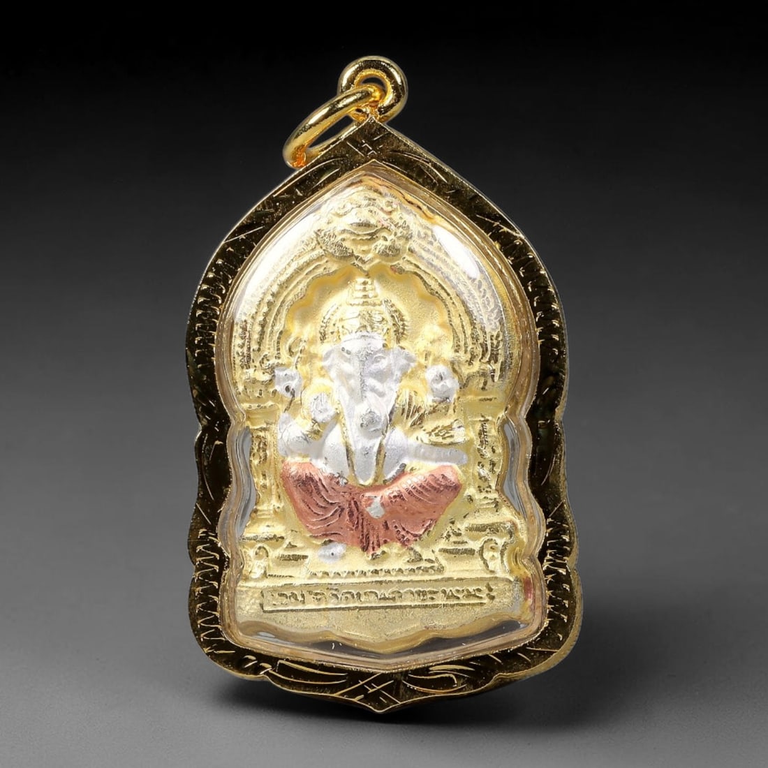 Thai Dual Deity Ganesha Votive Amulet - Gold Cased Pendant, 16YY: Ornate teardrop-shaped devotional pendant set within scroll-engraved polished gold casing with clear protective cover and integrated suspension loop. One side features silver-toned four-armed Ganesha 