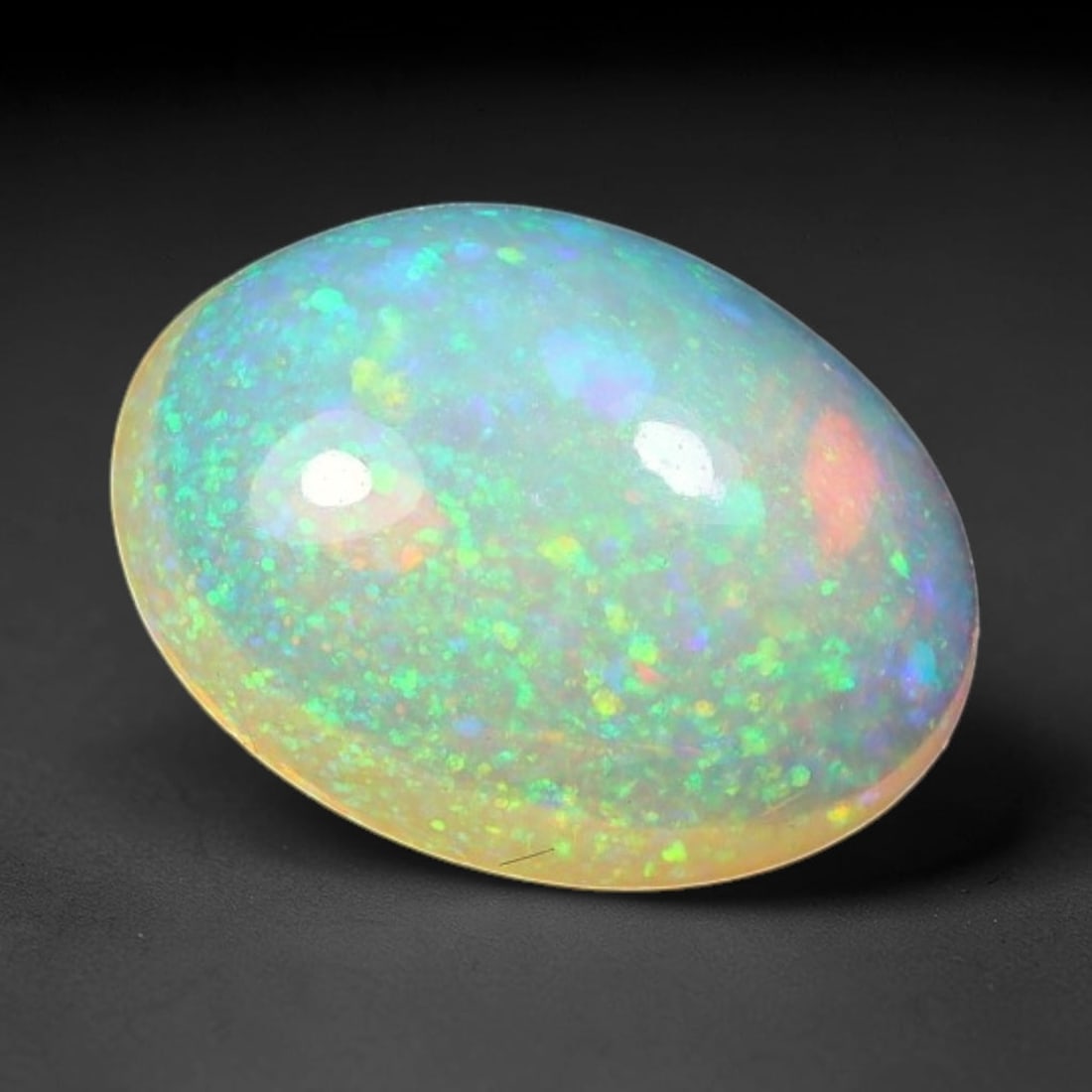 1.67ct Natural Ethiopian Welo Solid Opal Cabochon, 85WW: Hand polished solid Ethiopian Welo opal cabochon exhibiting dazzling multicoloured play of colour scattered evenly across the gemstone surface, set against a translucent pale base tone. The stone feat