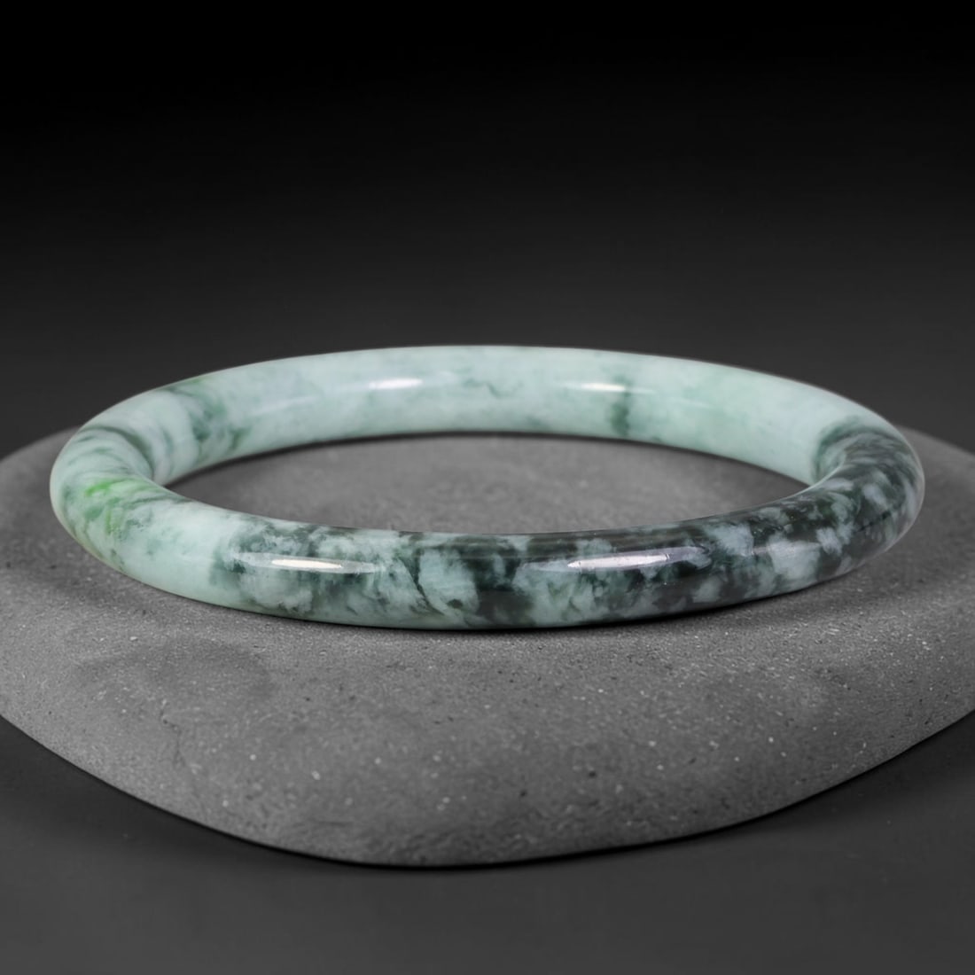 Natural Burmese Type A Jadeite Jade Bangle Bracelet, 15TD: Crafted from natural Burmese type-A jadeite, this slender bangle carries dynamic flowing dark forest-green and near-black cloudlike suffusions over a pale mint-green base, with small vivid bright gree